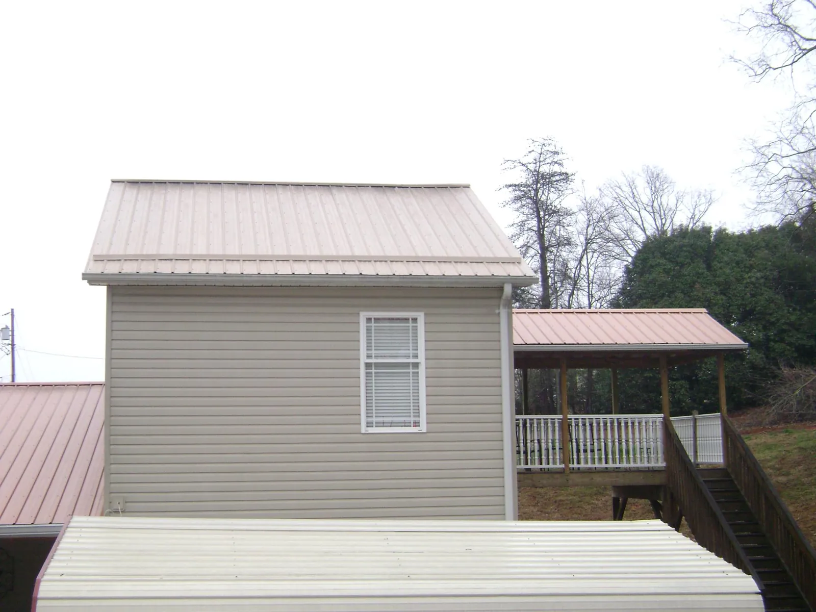 Tan metal roofs on a two story addition and attached porch, from a Roof Replacement job in Athens